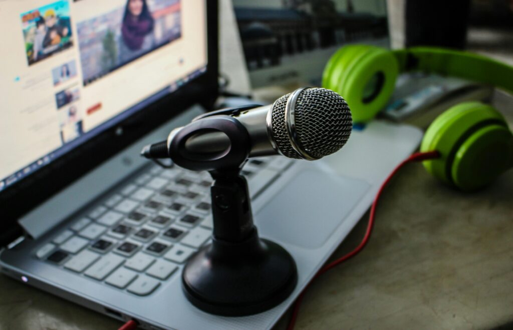 Close-up of a podcasting setup with a microphone, laptop, and green headphones.